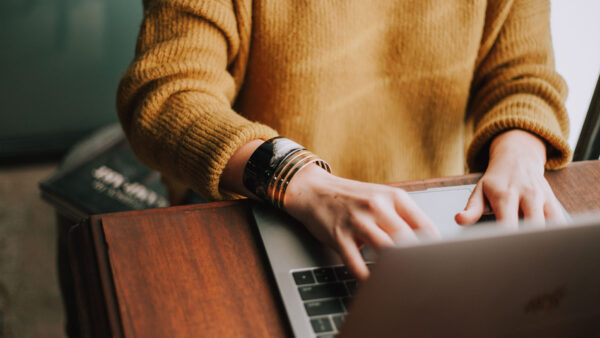 Person sitting at wooden table working on laptop.