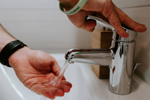 Person rinsing their hands under silver faucet.