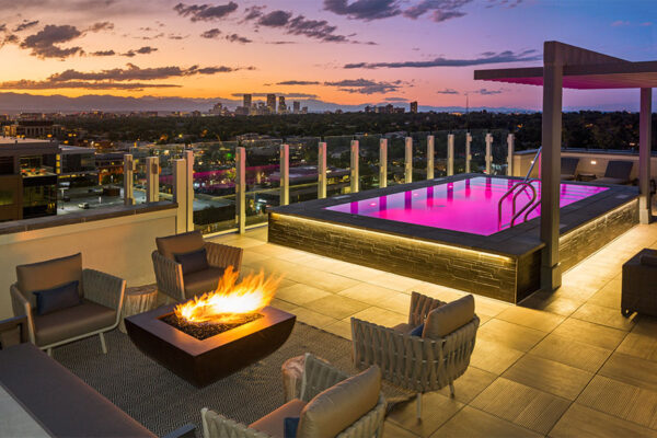 Rooftop patio with comfortable chairs, fire pit, and pool with purple lights.