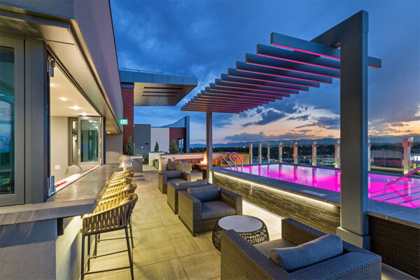 Rooftop patio with comfortable chairs, bar area, and pool with purple lights.
