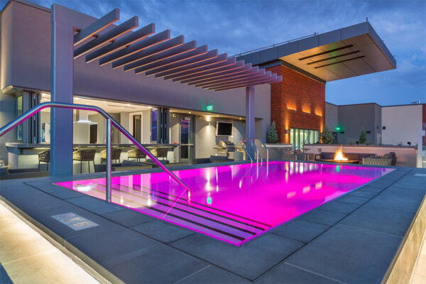 Rooftop patio with comfortable chairs, fire pit, and pool with purple lights.