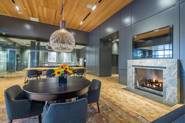 Lounge with wood floor, large rug, round table with chairs, and fire place.