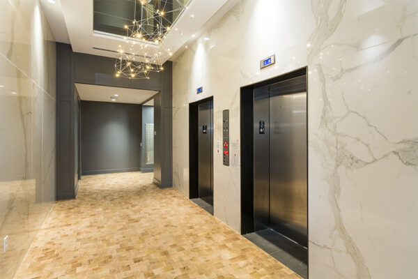 Elevator lobby with wood floor, geometric chandelier, and two elevators.