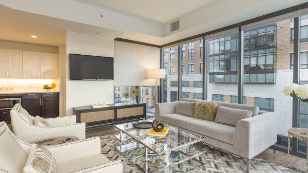 Living room with modern furniture, bar area, wall mounted TV, and floor to ceiling windows.