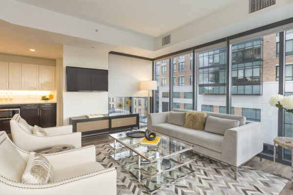 Living room with modern furniture, bar area, wall mounted TV, and floor to ceiling windows.
