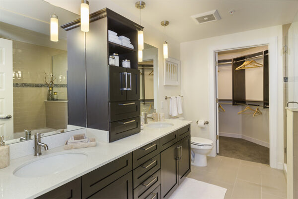 Bathroom with tile floor, dark cabinets, large mirrors, and door to closet.